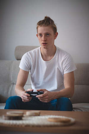 Focused expression of a man aged 20-29 with blond hair. The player sits on the couch in the living...