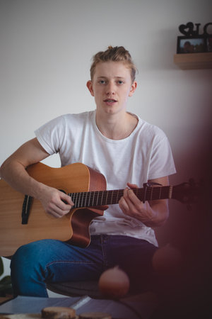 portrait of a blond singer sitting on a low stool strumming a guitar and singing a beautiful...