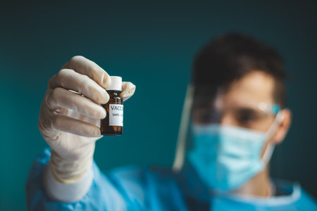 doctor in a protective shield, veil, and sterile gloved suit holds a single weapon against the...