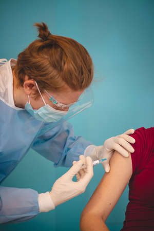 scientist in a protective suit injecting a syringe with a substance against the exact type of disease. Volunteer on tests. complementary treatment. A new type of treatment. Global pandemic.の写真素材
