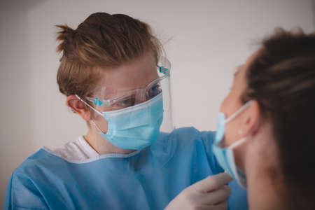 doctor in a sterile and protective suit takes a sample to assess positivity at the collection center. Swab from the patient's nose. Girl in a red T-shirt on a  test.の写真素材