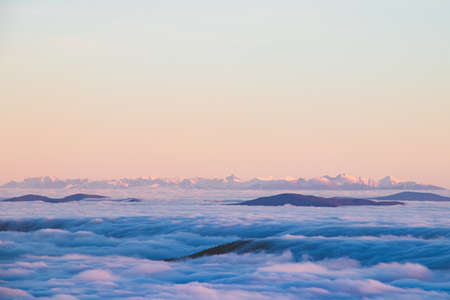 View of the High Tatras in Slovakia, which rise above the clouds and are covered with snow. View from Lysa Hora. Sunset with snowy hills. The sea of clouds floats in the wind.の写真素材