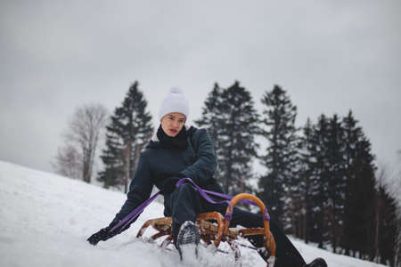 Teenager caught riding on a wooden sledge trying to adjust his direction with his hand and concentrating on his ride. In winter, the athlete goes down the piste on a historical object.の写真素材