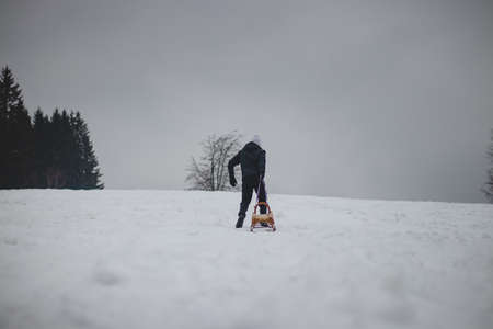 young boy of European descent in black clothes and a white cap goes uphill and pushes a wooden...