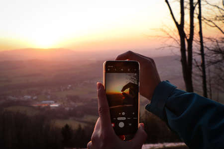 phone holder is trying to take a picture of his fingers holding the sun. Modern technology used to maintain momentum. Pocket little friend for every occasion. Sunset at Beskydy mountains.の写真素材