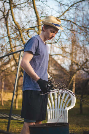 Hardworking man in work clothes uses loppers to split wood into smaller sticks to fit into the kiln for burning. Work in the garden. Grooming the plot. Beautifying the orchards.の写真素材