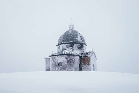 Hitoric chapel on Mount Radhost in Pustevny in Beskydy mountains in the east of the Czech Republic. Minimalism. The chapel rises out of the white mist. Wooden Catholic chapel shaved by frost and snow.の写真素材