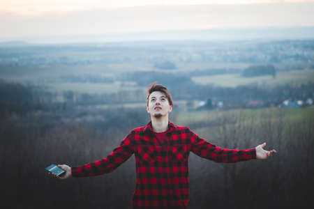 Candid portrait of a man in his 20s dressed in a black and red checked shirt joyfully facing the sky. He gives thanks to be on earth. Authentic people at their emotions.の写真素材