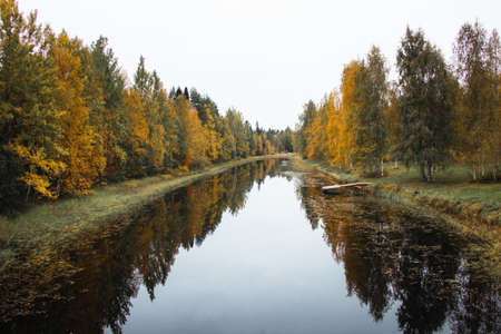 Autumn fairy tale in Kainuu, Finland. The colorful deciduous trees play with all their colors and reflect on the lake surface on a cloudy day. Orange, Green, blue colors.の写真素材