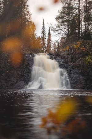 Famous Komulankongas waterfall, in Hyrynsalmi, Finland. Long exposure of the waterfall through orange-red leaves. Dramatic scene from the Kainuu region. The beauty of Finnish nature.の写真素材