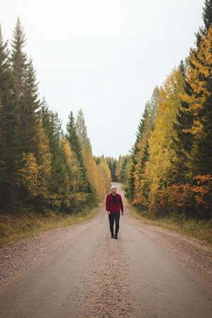 Man aged 23 wearing a checked red and black shirt walks along a foamy path surrounded by beautiful deciduous trees colored in autumn colors. Enjoy the moment. Kainuu region, Finland.の写真素材