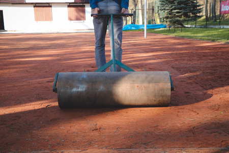 janitor smoothes the clay on the volleyball court with a large roller. Preparing the court for the new season. Spring workの写真素材
