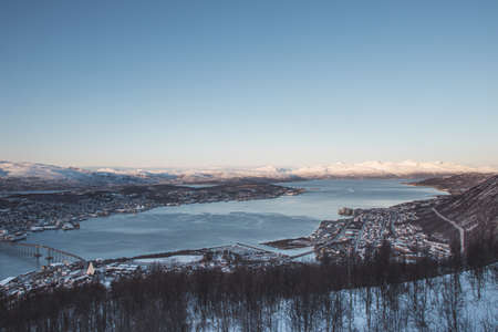view of the polar town of Tromso in northern Norway and the snowy hills in the background at sunset. Orange-red color lines rocky mountains. Exploring the world. A Scandinavian city and beauty of nature.の写真素材