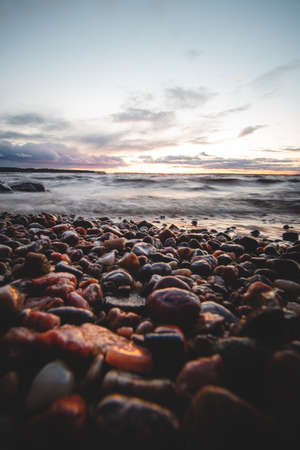 Dramatic sky with a mix of red, orange and purple over the waves of Lake Oulujarvi with detail on the colored pebbles on the beach at Kajaani, Kainuu region, Finland. Scandinavian sunset.の写真素材