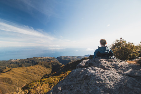 Blonde hiker takes a break on a rock overlooking the Atlantic Ocean and the Madeira Valley from the slopes of Pico Ruivo on the Portuguese island. Take a seat.の写真素材
