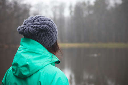 Brunette in winter jacket looking at a small pond near Opava, Czech Republic. Green and blue winter jacket. Lifestyle.の写真素材