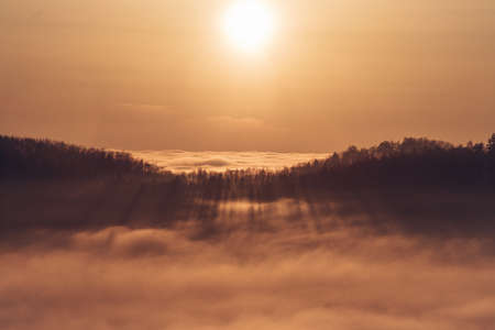 View of the sunset over a sea of clouds with a view of the sun passing through the forest on the other hill. Palkovicke hurky, Moravian-Silesian region, Czech Republic.の写真素材