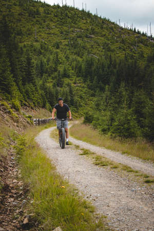 Swarthier type of person rides a downhill mountain scooter on a steep forest path around a mountain in Jeseniky mountains, Czech Republic. Dolni Morava resort.の写真素材