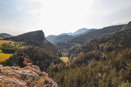 View of a tourist and the Kalte Rinne railway viaduct and a passing train in the Semmering area, Rax-Schneeberg Group in Styria, Austria.の写真素材