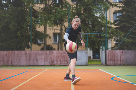 Basketball player controls and dribble the ball during a casual game on an outdoor court, bending down in focus. The court is surrounded by trees and nature, giving a peaceful and athletic atmosphere.の写真素材