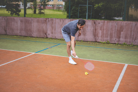 Badminton player stretches to retrieve a low shuttlecock during an intense game on an outdoor court....