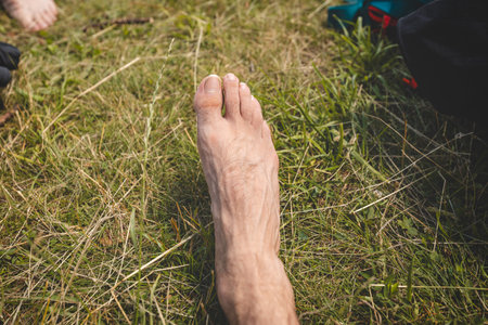 Bare feet stand on sunlit, dry grass, symbolizing a connection to nature, simplicity, and grounding during a serene moment in the Beskydy Mountains, Czech Republic.の写真素材