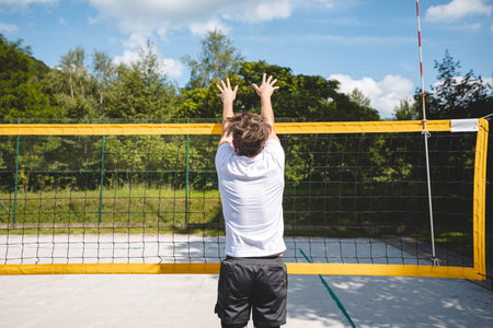 Volleyball player jumping to block a volleyball at the net on a sand court. The outdoor scene captures the intensity of summer sports and beach volleyball.の写真素材