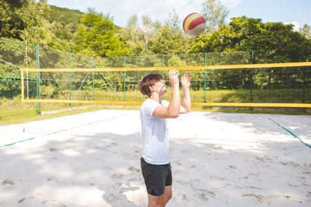 Volleyball player standing on a sand court, holding a ball and preparing for the next play during a quiet moment in an outdoor beach volleyball match.の写真素材