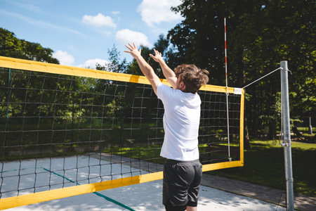 Volleyball player jumping to block a volleyball at the net on a sand court. The outdoor scene captures the intensity of summer sports and beach volleyball.の写真素材