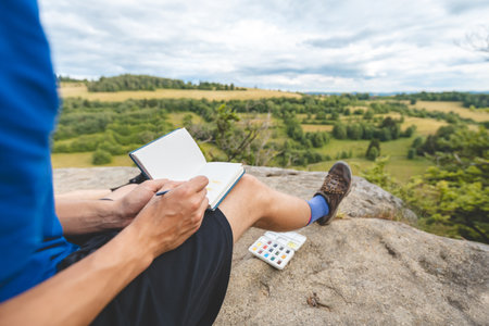 Young artist, sitting on a rock surrounded by lush forest, paints in a notebook with watercolors during a serene outdoor creative moment.の写真素材
