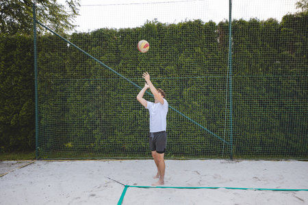 Volleyball player serving a volleyball on a sand court under a bright blue sky. A dynamic outdoor scene, perfect for summer sports and beach volleyball enthusiasts.の写真素材