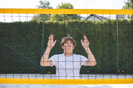 Volleyball player standing face-to-face with the net on a sand court, focused and preparing for the...