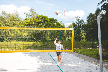 Volleyball player jumping to hit the ball over the net on a sand court during an outdoor game. The action captures the intensity and athleticism of beach volleyball.の写真素材