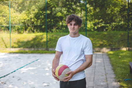 Volleyball player standing on a sand court, holding a ball and preparing for the next play during a quiet moment in an outdoor match.の写真素材