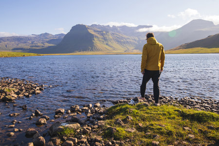 Man in a yellow jacket stands barefoot on the rocky shore of a serene lake on the Snaefellsnes Peninsula in western Iceland. Enjoying the purity of nature.の写真素材