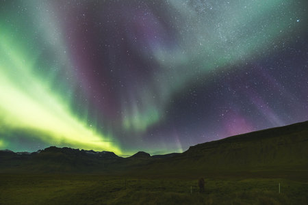 Aurora borealis, northern lights, stretches across the entire night sky in various colors above the rocky volcanic mountains on the Snaefellsnes peninsula in West Iceland. A nighttime fairy tale.の写真素材