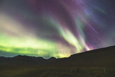 Aurora borealis, northern lights, stretches across the entire night sky in various colors above the rocky volcanic mountains on the Snaefellsnes peninsula in West Iceland. A nighttime fairy tale.の写真素材