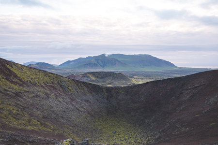 Volcanic landscapes of the Snaefellsnes Peninsula in Iceland, with vast craters, rugged terrain, and distant green mountains under a cloudy sky.の写真素材