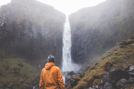 Traveler in an orange jacket stands in awe before Grundarfoss waterfall on the Snaefellsnes...
