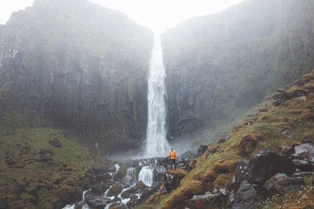 Traveler in an orange jacket stands in awe before Grundarfoss waterfall on the Snaefellsnes...