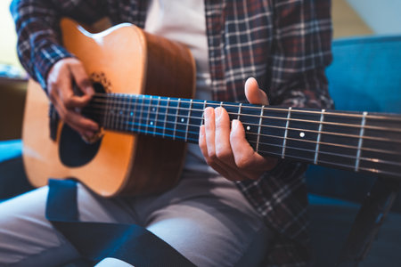 Close-up of a musician playing an acoustic guitar, fingers pressing on the fretboard, evoking a sense of creativity, passion, and emotional connection through warm, resonant tones.の写真素材