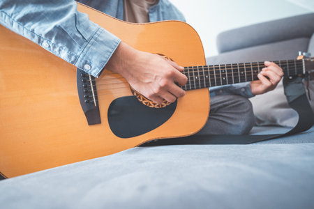 Relaxing on a cozy sofa, a man gently strums his acoustic guitar, lost in music. A peaceful home...