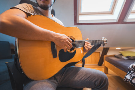 Man alone in the middle of a sunlit room enjoys playing a beautiful wooden acoustic guitar and...