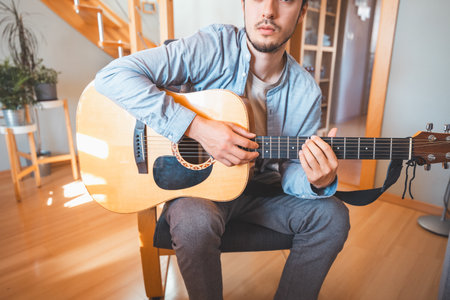 Man alone in the middle of a sunlit room enjoys playing a beautiful wooden acoustic guitar and...