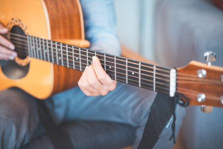 Close-up on a musician strums an acoustic guitar in a cozy home, immersed in music. His casual...
