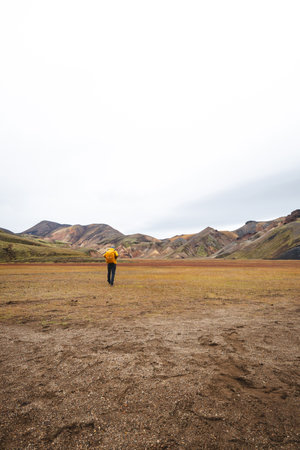 Traveler walks through a rugged lava field in the Icelandic Highlands, surrounded by mossy rocks and distant rhyolite peaks. A surreal journey through Iceland's wild heart.の写真素材