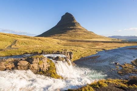 Kirkjufell mountain at sunrise with golden grasslands and soft clouds above, creating a peaceful and iconic Icelandic scene on the Snaefellsnes Peninsula.の写真素材