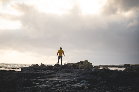 Young traveler walks along a rocky beach during a breathtaking stormy sunset in western Iceland, enjoying the last rays of sunlight. Dramatic sky and soft Arctic light.の写真素材