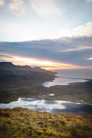Golden sunrise lights up the fjords and valleys below Kirkjufell Mountain, Iceland, as reflections...