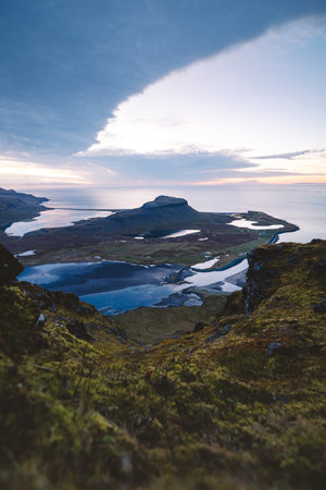 Breathtaking sunset view from the top of Kirkjufell Mountain in Iceland, revealing coastal fjords, farmland, and mirror-like water beneath dramatic Arctic skies.の写真素材